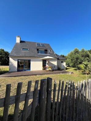 Ein Haus mit einer Terrasse, einem eingezäunten Garten und blauem Himmel.