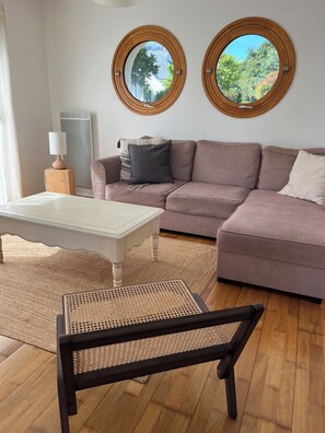 Ein Wohnzimmer mit einer Couch, zwei runden Fenstern, einer Lampe und einem Sessel.