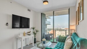 Un salon moderne avec un canapé vert, une table basse en verre et un téléviseur fixé au mur.