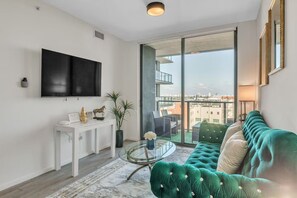 A modern living room with a green sofa, a glass coffee table, and a TV mounted on the wall. - Infinity Pool - Modern Luxury - Spacious 2BR - Gym (Miami)