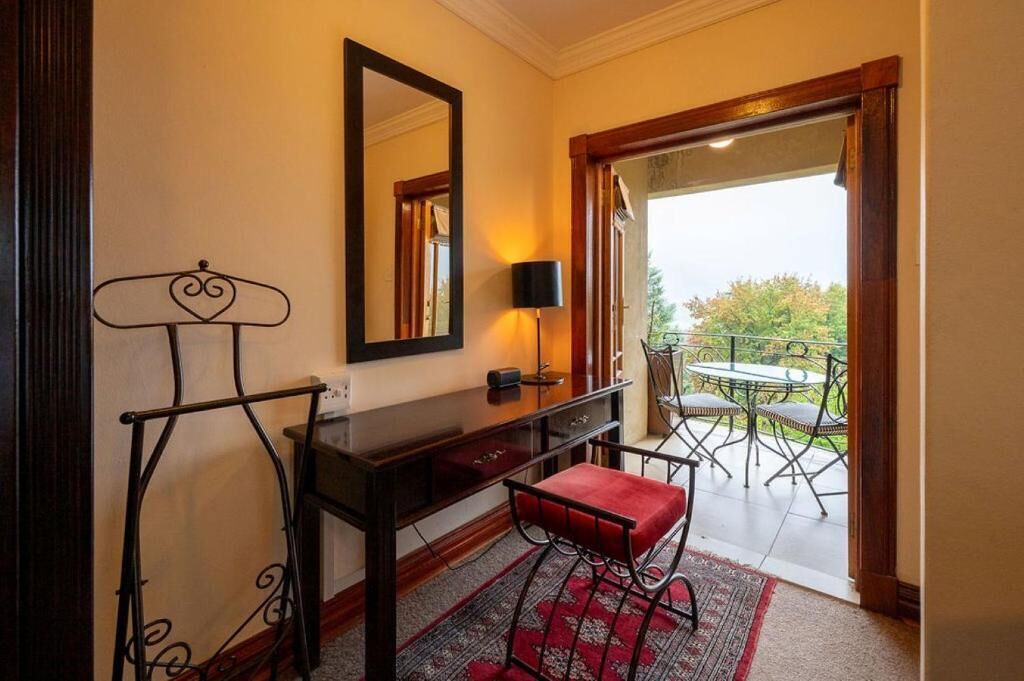A room with a desk, a chair, a mirror, a lamp, and a view of an outdoor patio with a table and chairs.