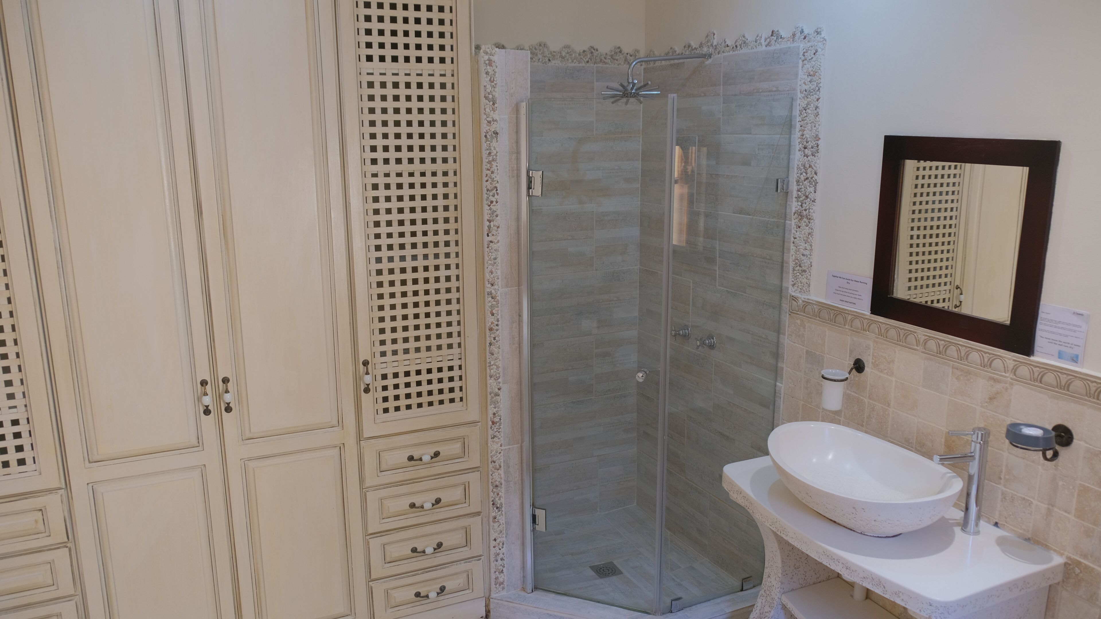 Casa de banho com cabine de duche em vidro, lavatório e espelho com moldura decorativa.