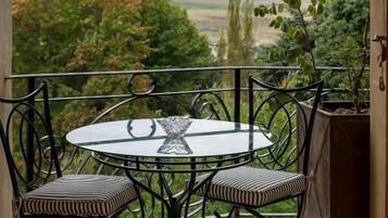 A balcony with a round table and chairs, a potted plant, and a view of mountains and trees.