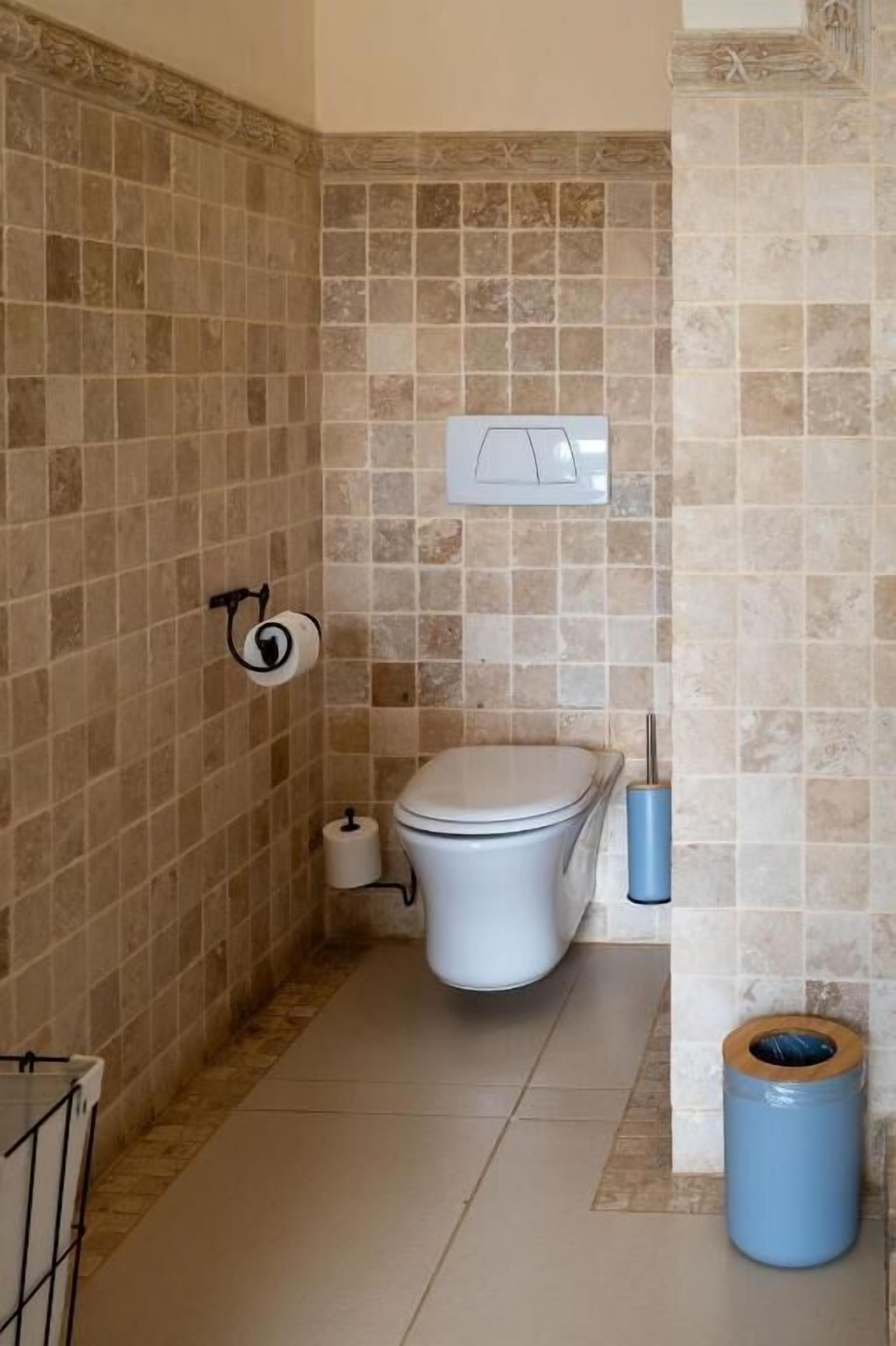 Et badeværelse med toilet, skraldespand og toiletpapirholder.