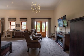 A spacious living room with a fireplace, a television, and a dining area with a kitchen counter. - IL Castello Boutique Hotel (Clarens)