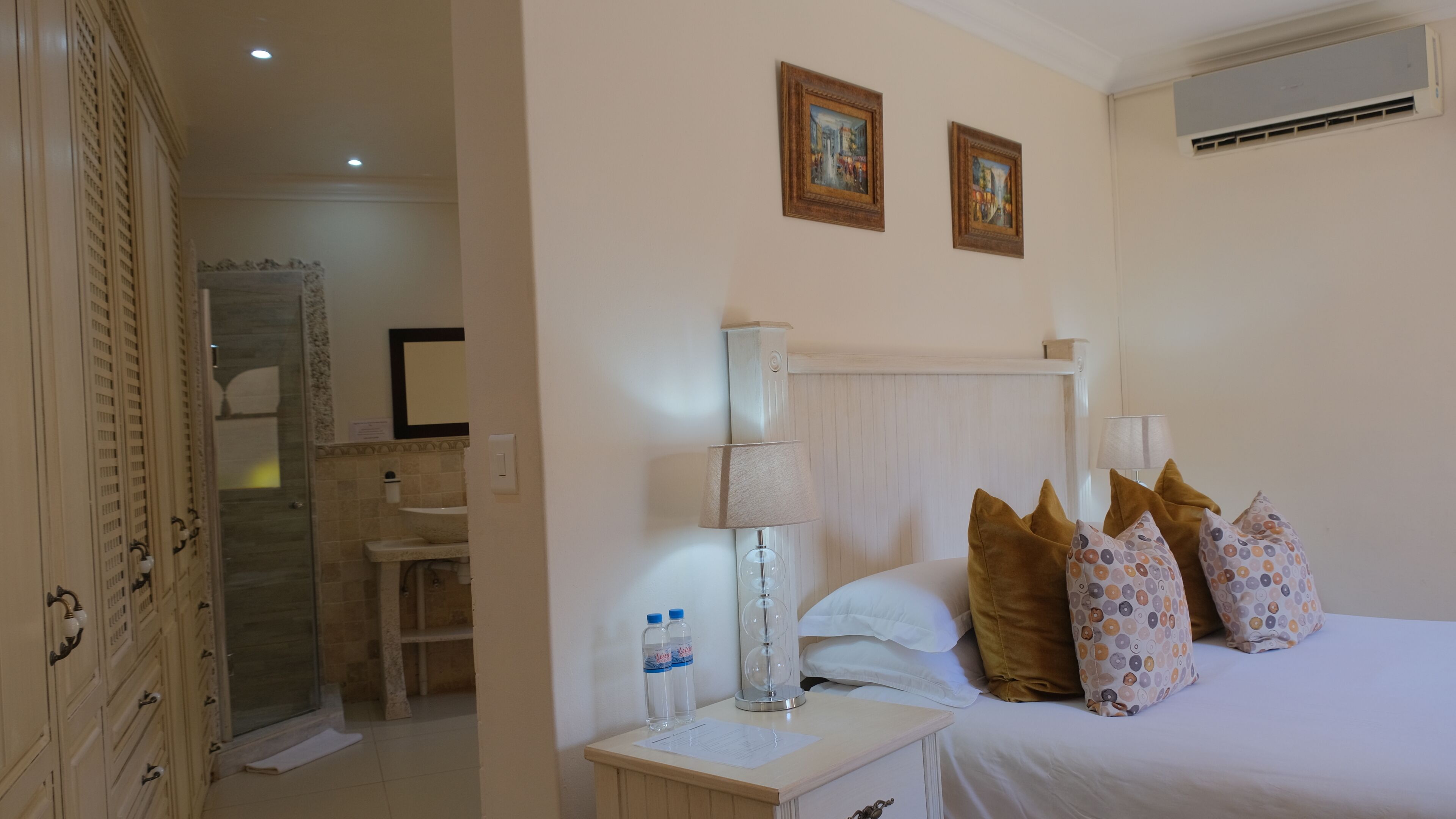 Camera d'albergo con un letto, cuscini, un comodino, una lampada, uno specchio e una zona doccia.
