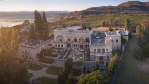 A large, historic building with multiple wings, a central courtyard, and a view of a lake and hills. - IL Castello Boutique Hotel (Clarens)