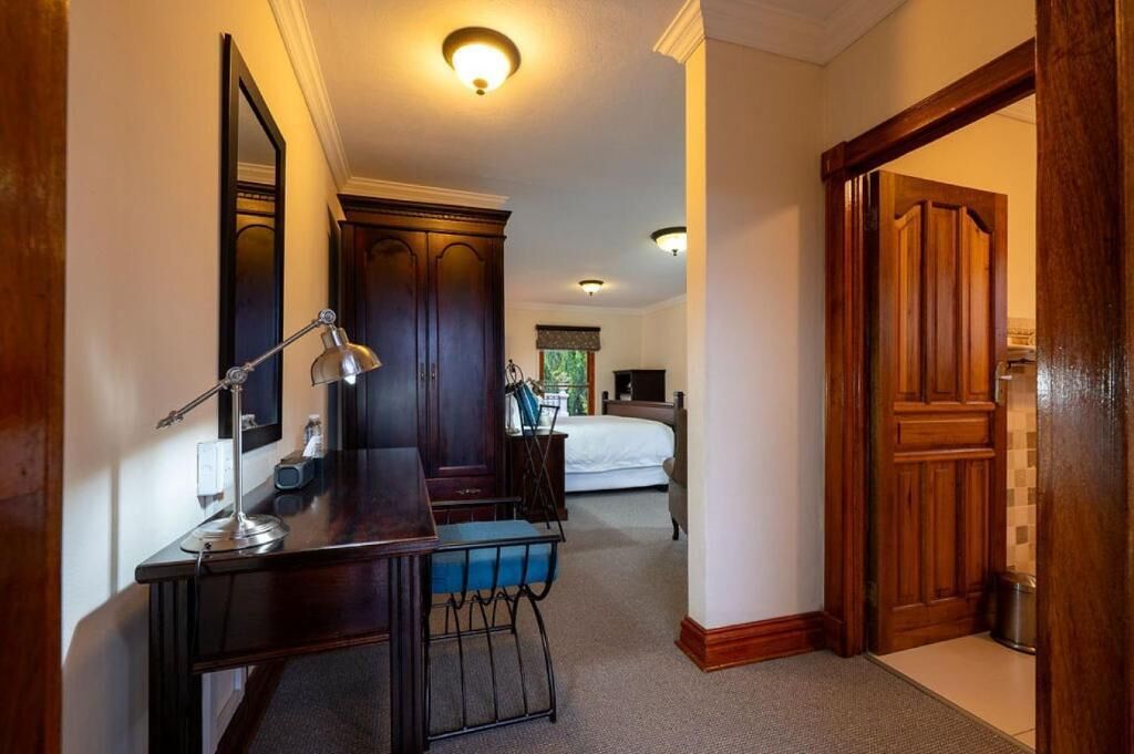 Quarto de hotel com escrivaninha, cadeira, cama e porta de madeira.