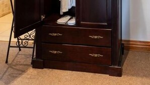 A dark wooden wardrobe with a mirror, a hanging robe, and a pair of shoes visible inside. - IL Castello Boutique Hotel (Clarens)