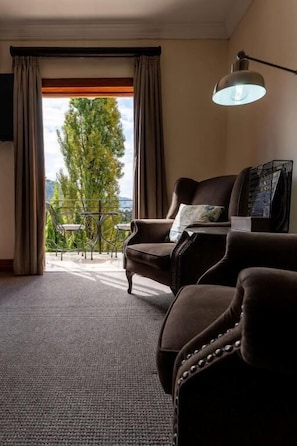 Une chambre d’hôtel avec vue sur les arbres, un balcon, un canapé, une table avec une lampe et un téléviseur.