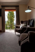 Habitación de hotel con vista a árboles y un balcón, un sofá, una mesa con lámpara y un televisor.