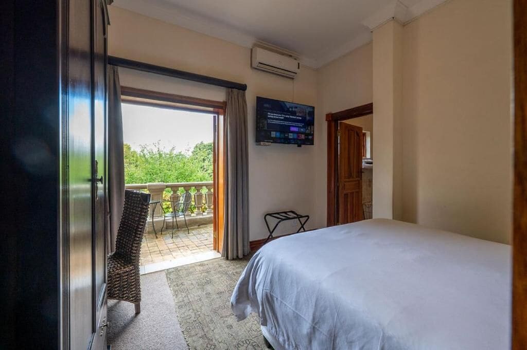 Une chambre d’hôtel équipée d’un lit, d’une télévision, d’un climatiseur, d’un balcon avec une chaise et offrant une vue sur la verdure.