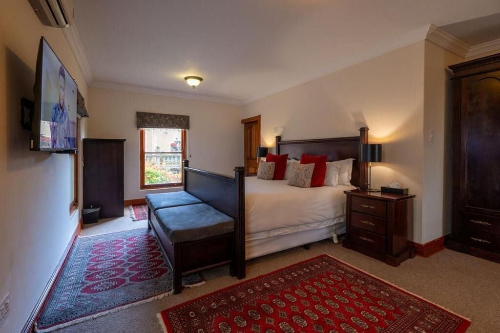 A bedroom with a bed, bedside table, lamp, and a TV mounted on the wall.