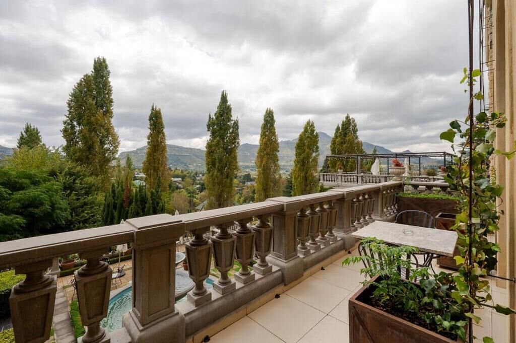 A balcony with a view of trees and mountains, a pergola, and a tiled floor.