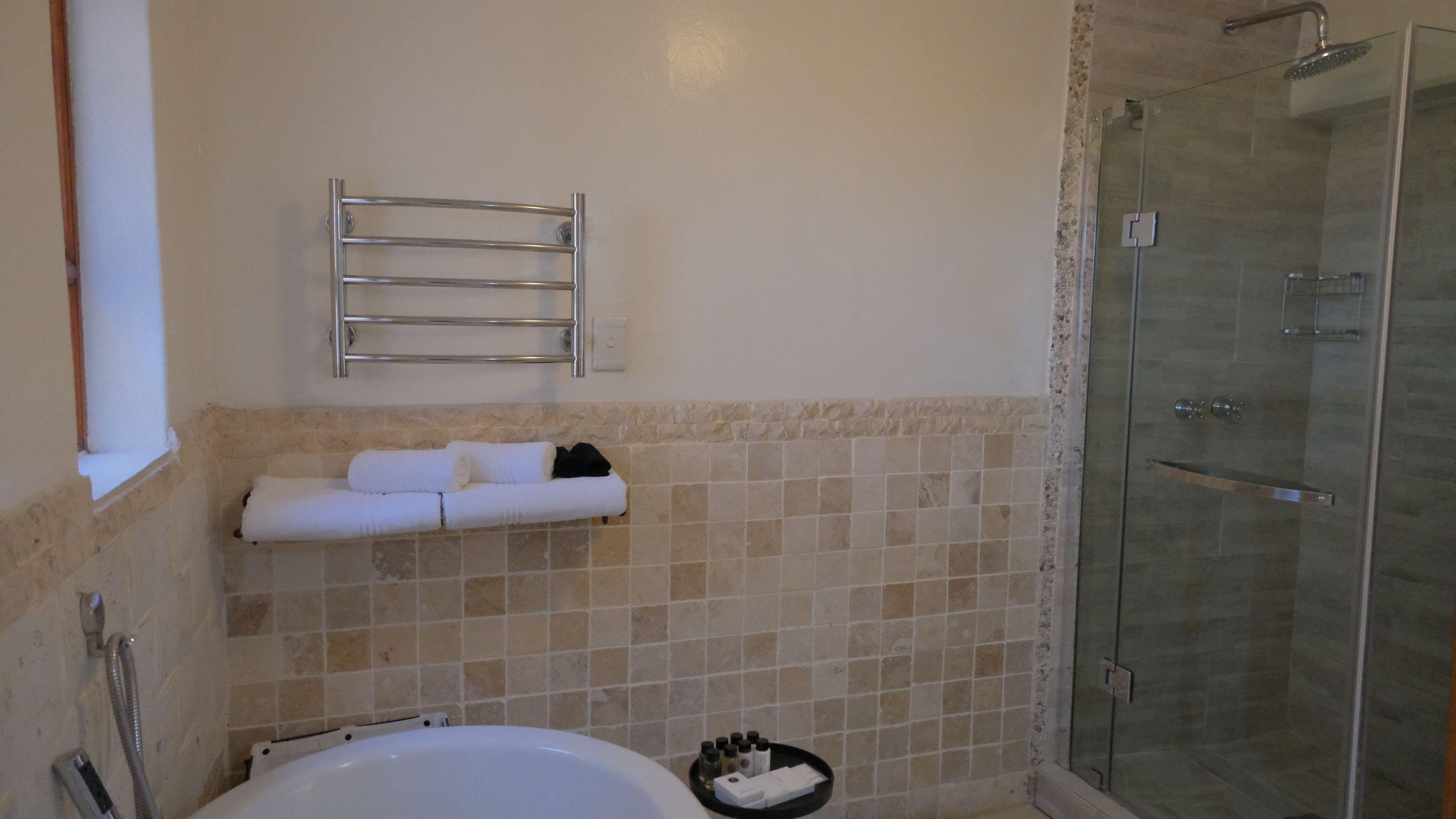 Un baño con bañera, cabina de ducha de vidrio, toallero y estante con artículos de aseo.