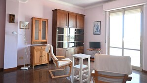 A living room with a wooden cabinet, a white armchair, a small table, a floor lamp, and a television. - Location: in a residential area, a few steps from the sea and all services.Description: apartment on the fourth floor of a building with lift. Living room with terrace overlooking the sea - bright kitchen with dining table and balcony - double bedroom wi (SENIGALLIA)