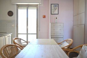 Un coin repas avec une table en bois et des chaises en osier, un buffet blanc et une porte donnant sur l’extérieur.