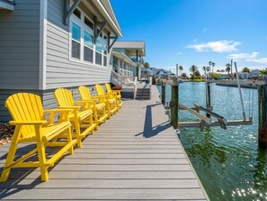 A wooden dock with yellow chairs, a building with a balcony, and a marina with boats. - The Salty Flamingo (Rockport)