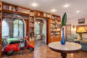 A library with bookshelves, a red scooter, a blue vase, and a round table. - L'Elisea Maison de Charme (Castellabate)