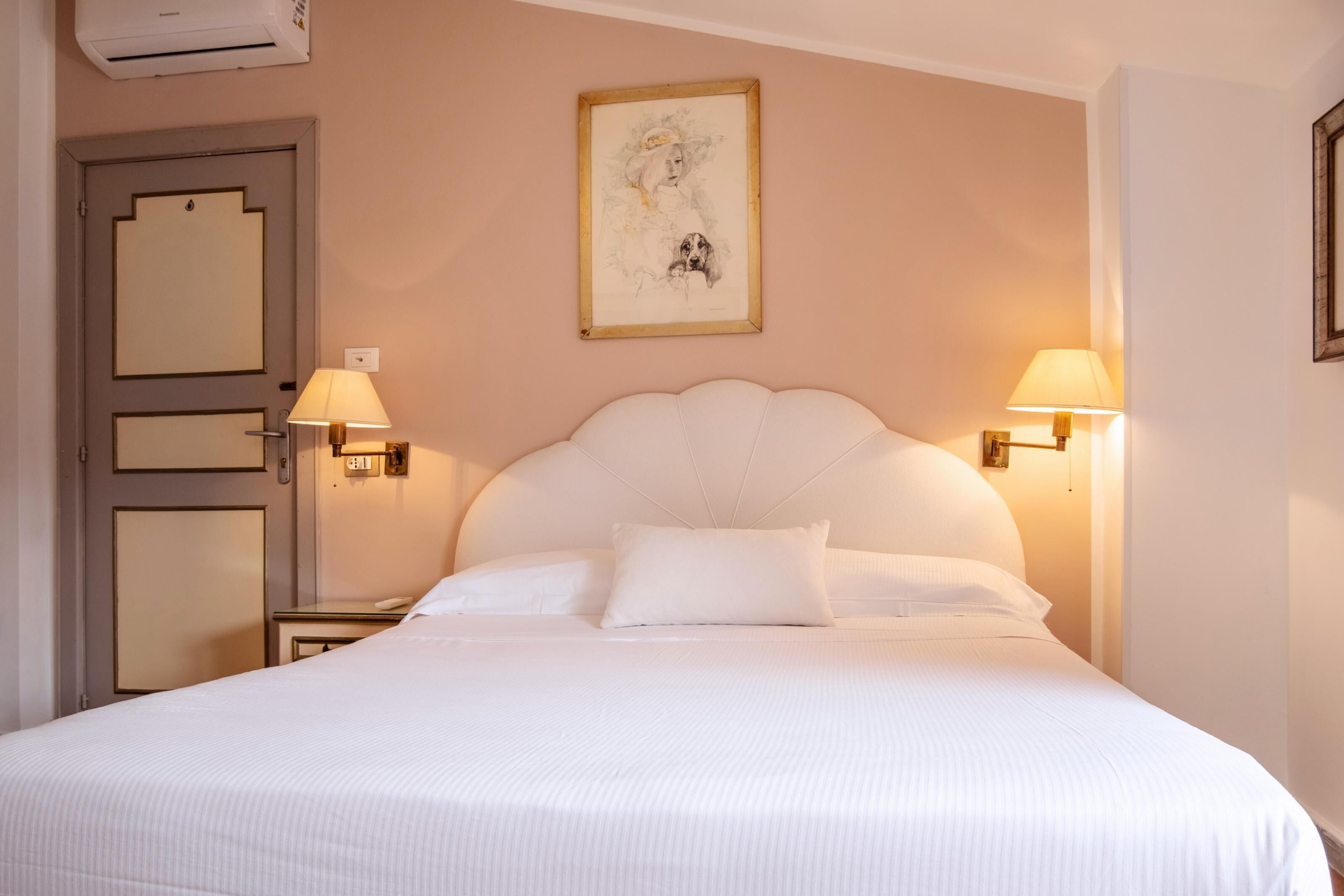 Ein Hotelzimmer mit einem großen Bett, zwei Nachttischlampen, einem gerahmten Kunstwerk an der Wand und einer Tür mit Lichtschalter.