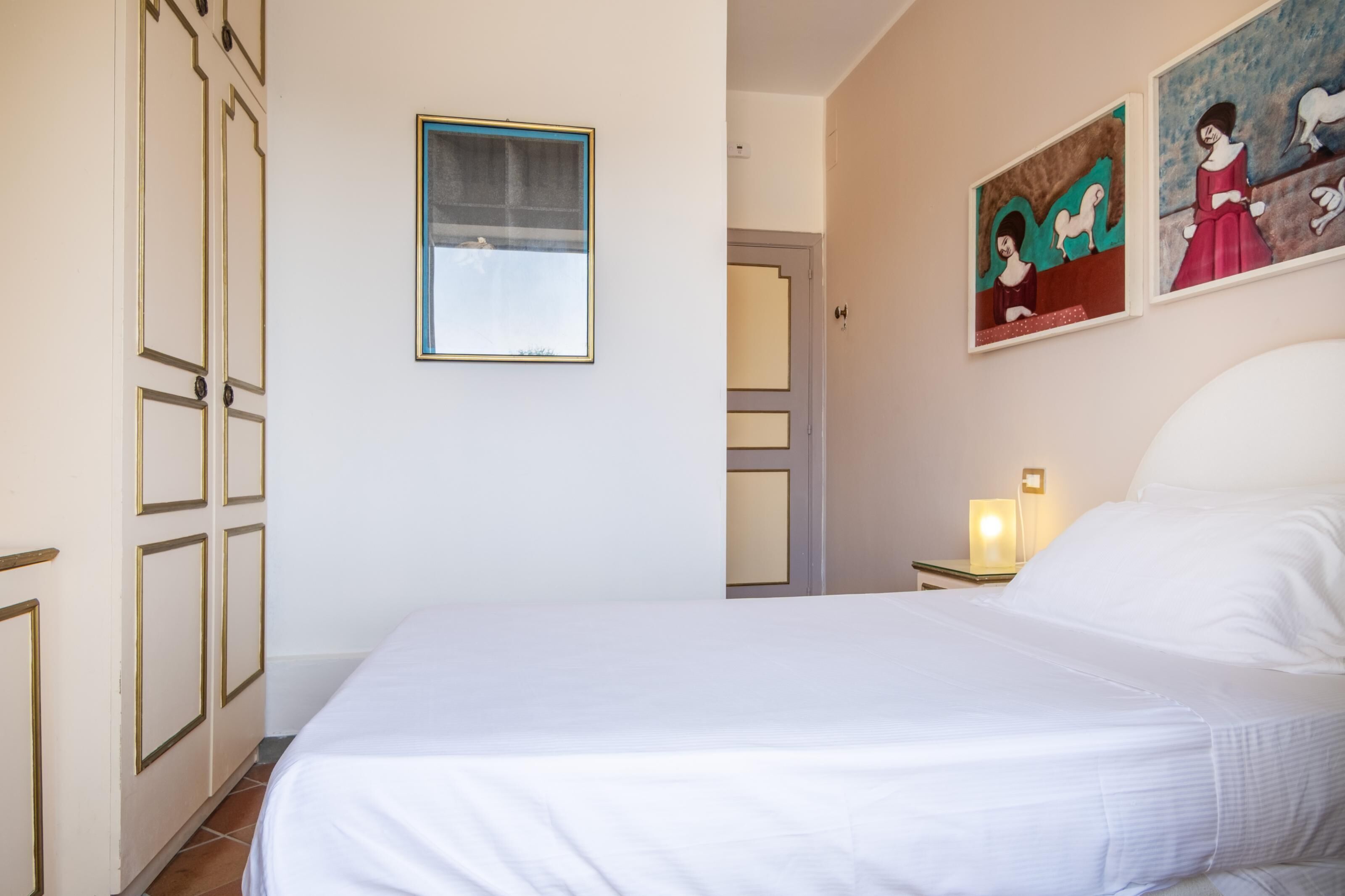 Une chambre à coucher avec un lit, une table de chevet avec une lampe, une porte et deux tableaux au mur.