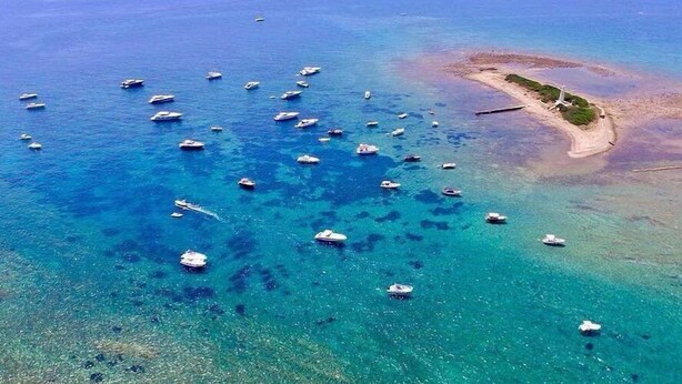 Vista aérea de una zona costera con numerosos barcos en aguas azul turquesa.