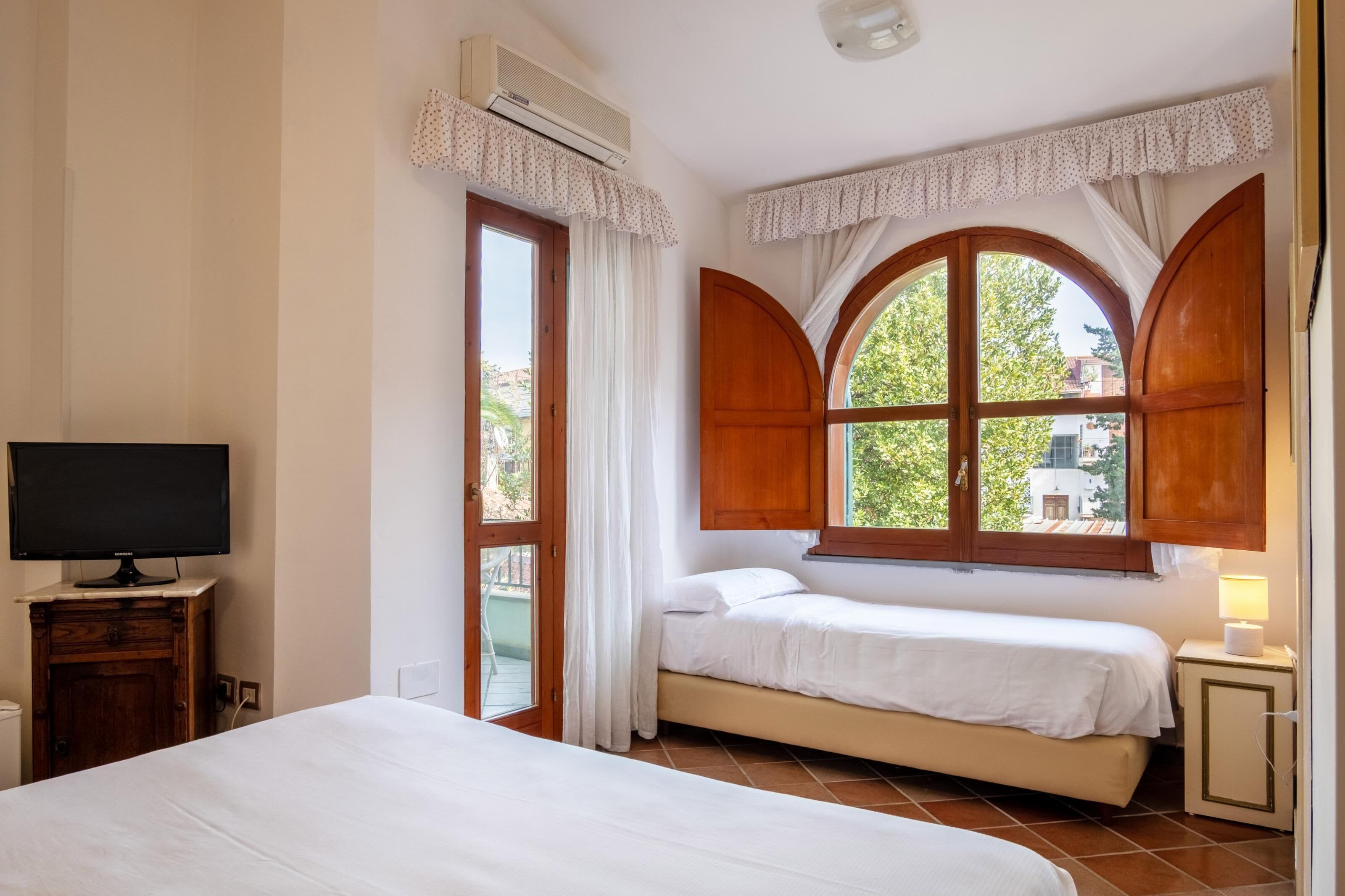A bedroom with a bed, a TV, an air conditioner, and a window with curtains.