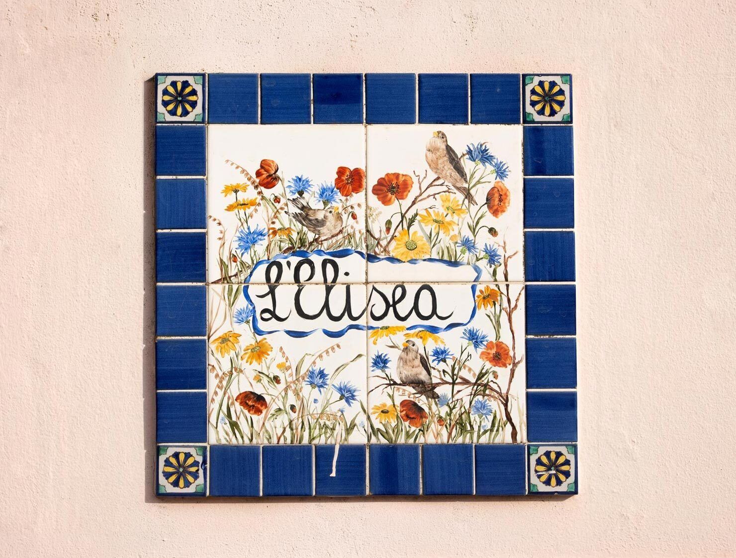 A decorative tile with floral patterns and the word 'L'ileuse' on a wall.