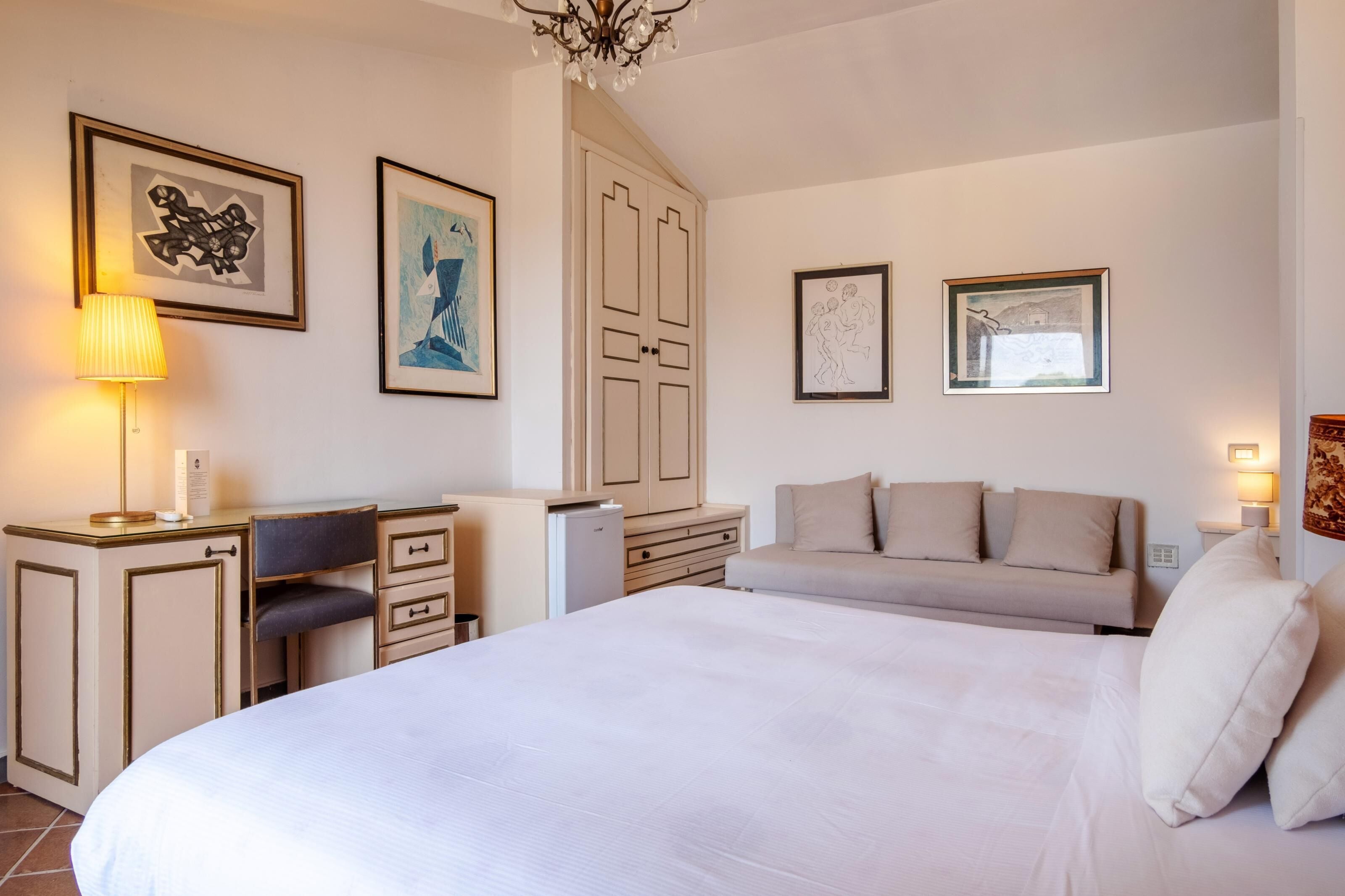 Una camera d'albergo con un letto, una scrivania, una sedia, un armadio e opere d'arte alle pareti.