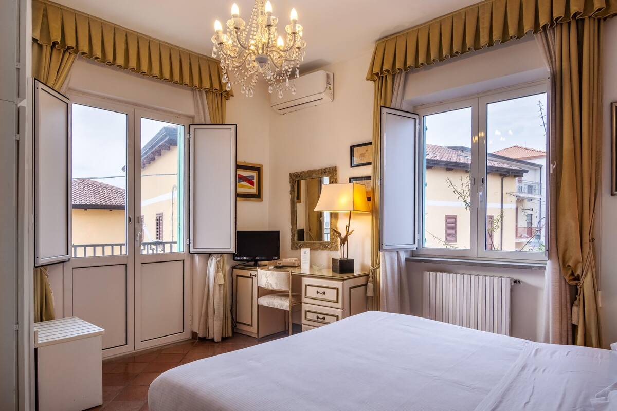 A hotel room with a bed, desk, chair, and a large window with curtains.