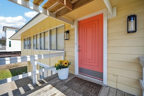 A yellow house with a red door, a white porch railing, and a welcome mat. - Salty Sandpiper (Rockport)