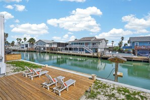 A waterfront property with a wooden deck, lounge chairs, and a dock extending into the water. - Salty Sandpiper (Rockport)