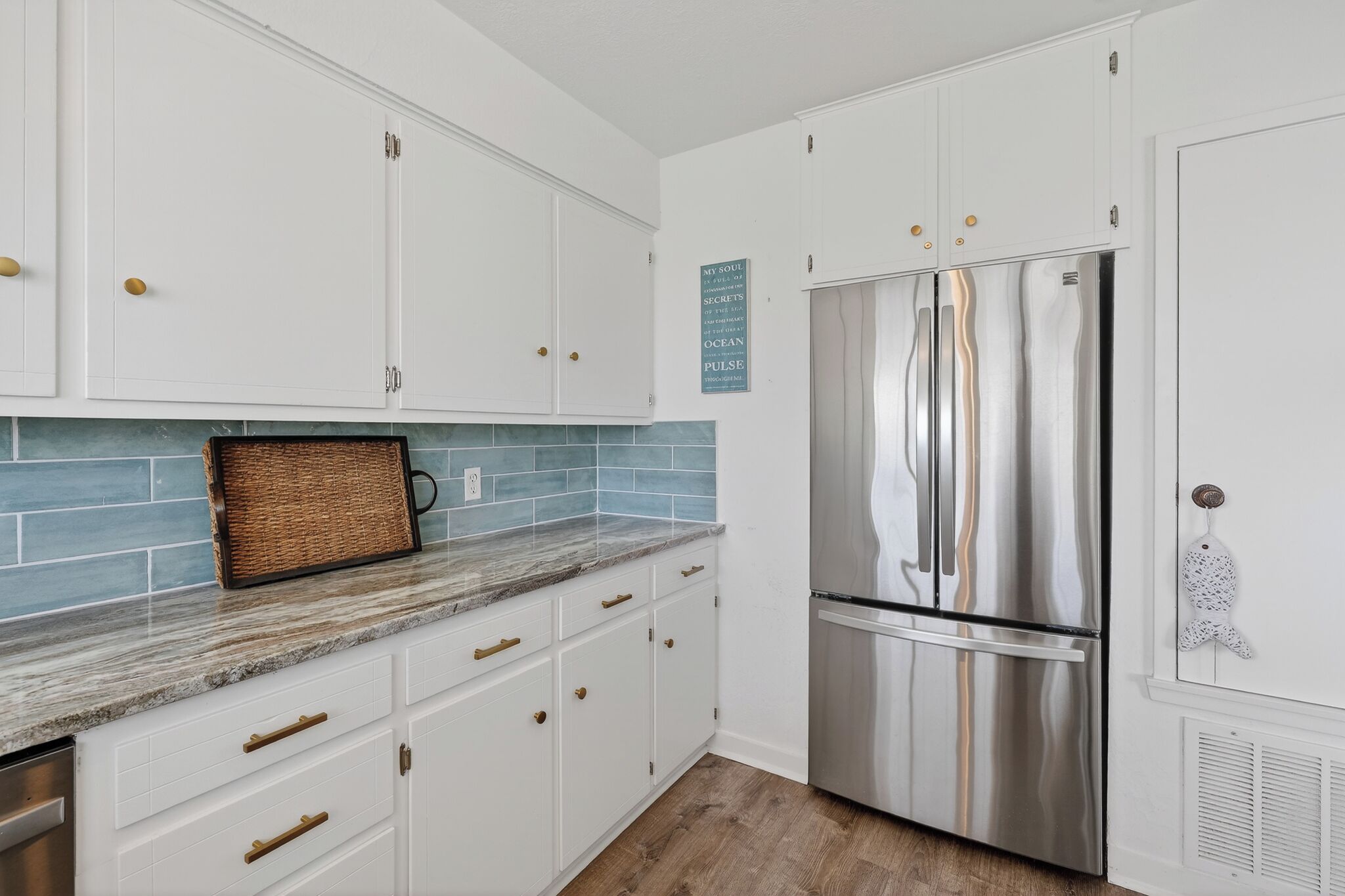 A kitchen with white cabinets, a stainless steel refrigerator, and a blue tiled backsplash.