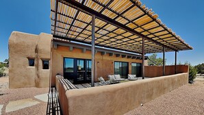 A modern house with a covered patio, outdoor seating, and a view of the desert landscape.