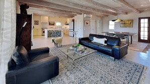 A spacious living room with a black leather sofa, a glass coffee table, and a patterned rug.