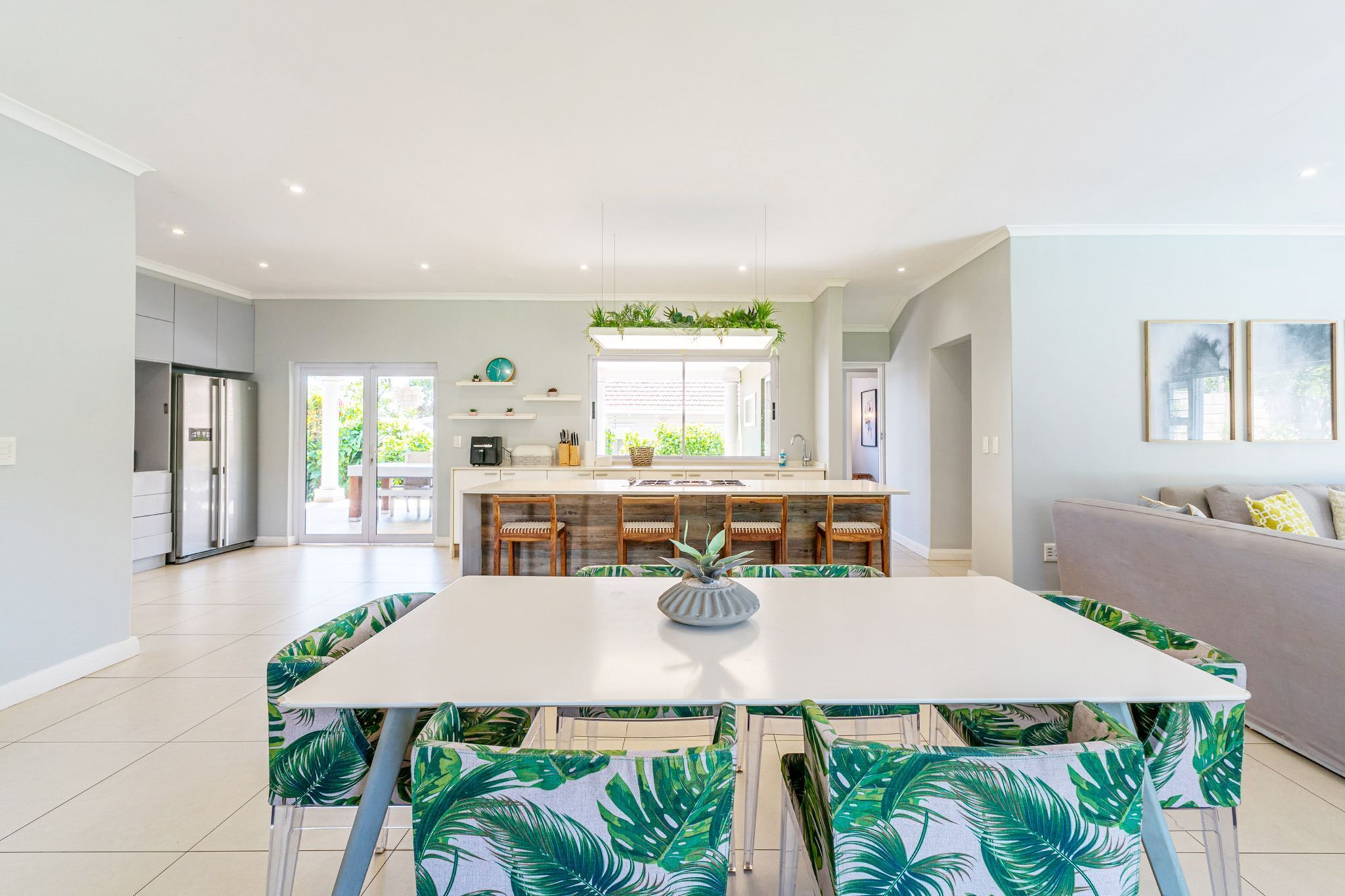 A modern kitchen with a central island, a dining area with a white table and chairs, and a grey sofa in a bright living space.