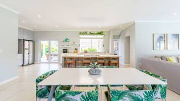 A modern kitchen with a central island, a dining area with a white table and chairs, and a grey sofa in a bright living space.
