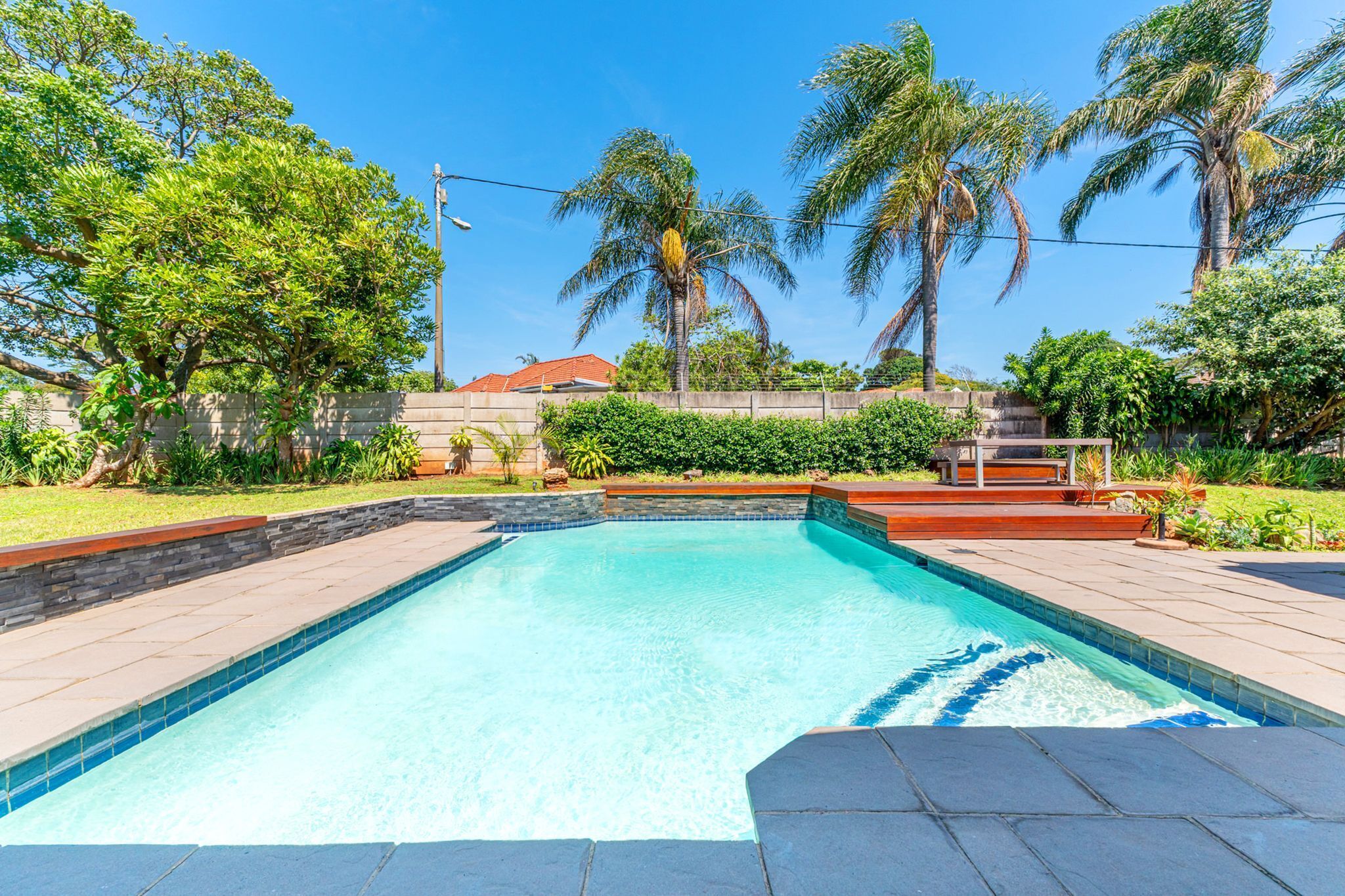 A rectangular swimming pool with a tiled edge, surrounded by a stone wall and a low brick border.