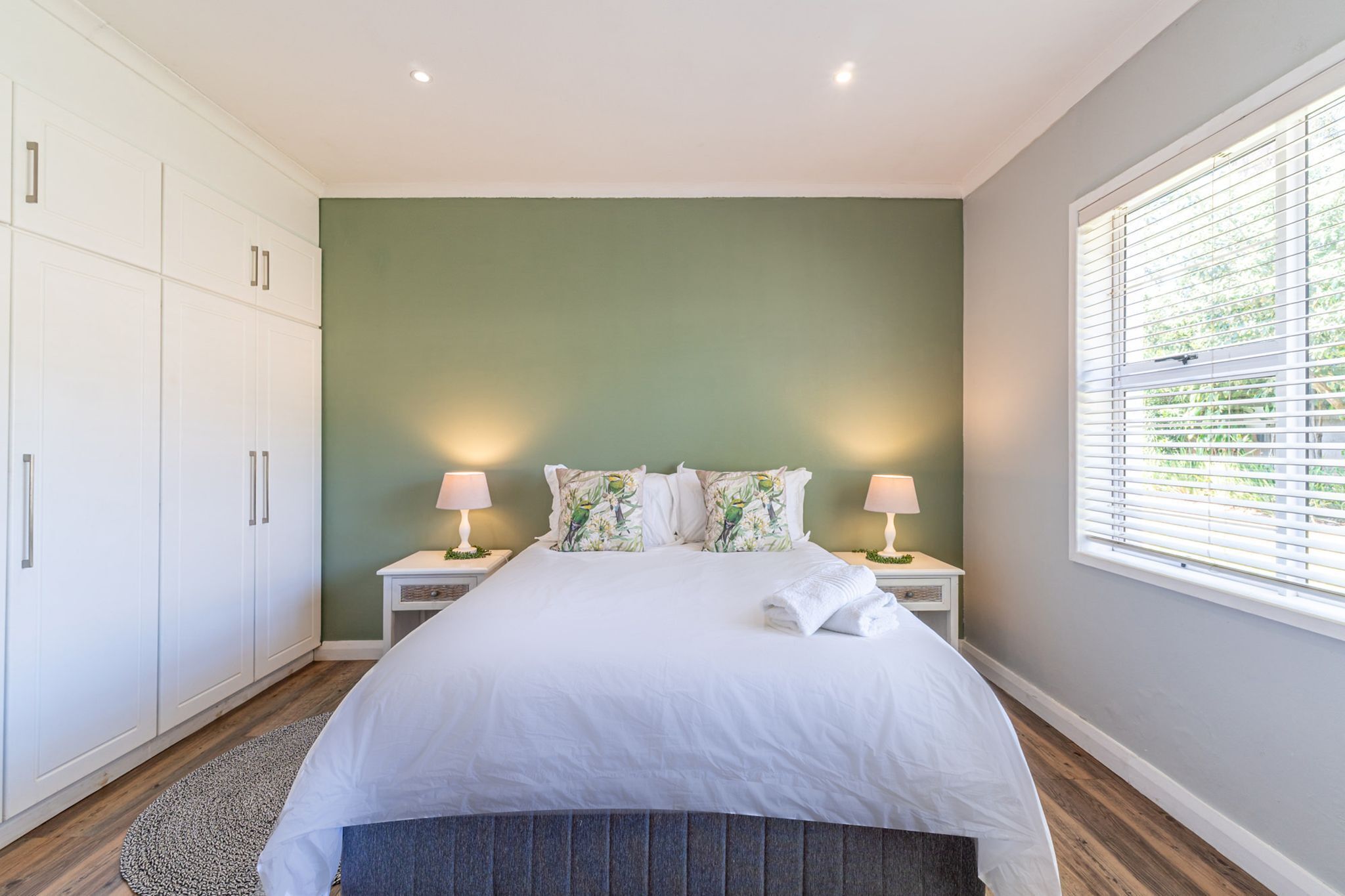 A bedroom with a bed, nightstands, a wardrobe, and a window with blinds.