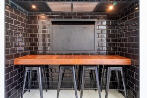A room with a long wooden table, black metal chairs, and a black tiled wall.