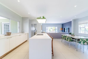 A modern kitchen with a central island, white cabinetry, and a dining area with a long table and chairs.