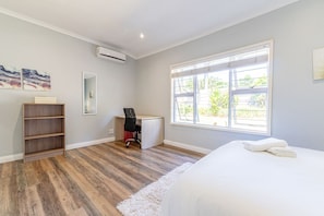 A bedroom with a bed, a desk, a chair, a bookshelf, and a large window.