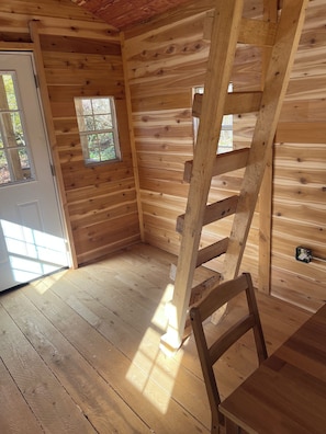 Het interieur van een houten chalet met een houten ladder, een deur en een raam.
