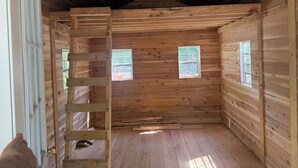 A wooden cabin interior with a loft area, two windows, and a door. - Peaceful & private 1 room cabin  
near stream/water (Smithville Flats)