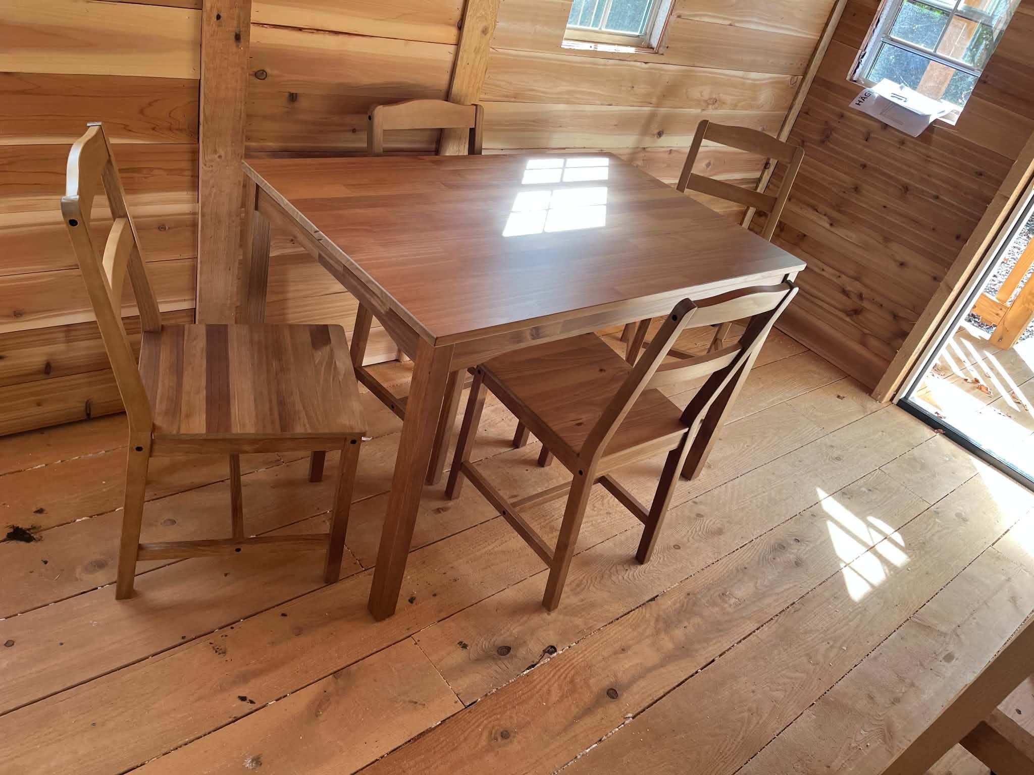 A wooden dining table with four chairs in a room with wooden walls and floors.