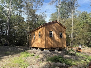 A wooden cabin with a gabled roof, two windows, and a small porch area.