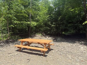 Een houten picknicktafel in een bebost gebied met een aarden ondergrond.
