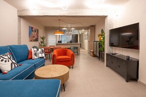 A modern living room with a blue sofa, orange armchair, wooden coffee table, and a TV mounted on the wall. - GuestReady - Stylish art and comfort Malaga centre (Málaga)
