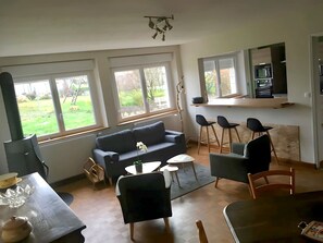 Ein modernes Wohnzimmer mit einer Couch, Sesseln, einem Esstisch und großen Fenstern mit Blick ins Freie.