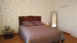 A bedroom with a bed, a round side table, a mirror, and a wall with a floral pattern.